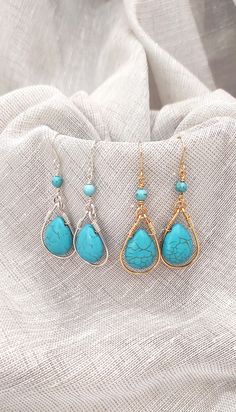 three pairs of earrings with turquoise stones and gold wire hanging from the ear hooks on top of a white cloth