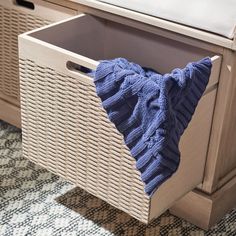 a blue blanket sitting on top of a white basket next to a wooden cabinet with drawers