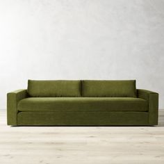 a green couch sitting on top of a hard wood floor next to a white wall