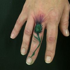 a person's hand with a green flower tattoo on the middle of their finger