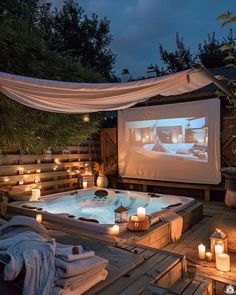 a hot tub sitting on top of a wooden deck next to a movie screen and candles