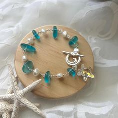 a bracelet with sea glass beads and charms on a wooden stand next to a starfish