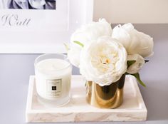 a candle and some white flowers on a marble tray in front of a framed photo