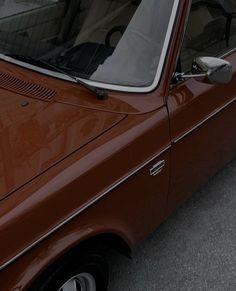 an orange car parked on the side of the road with a dog in it's window