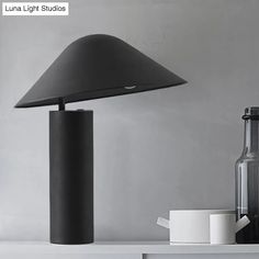 a black lamp sitting on top of a table next to a white cup and bottle