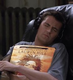 a man laying in a chair with headphones on his ears and holding a book