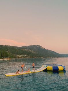 two people and a dog on a surfboard in the water with mountains in the background