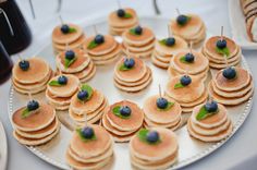 small pancakes with blueberries and mint are arranged on a white plate next to other desserts