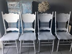 four white chairs sitting next to each other in front of a blue cabinet and wall