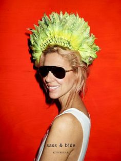 a woman in sunglasses and a yellow flowered headdress stands against a red wall