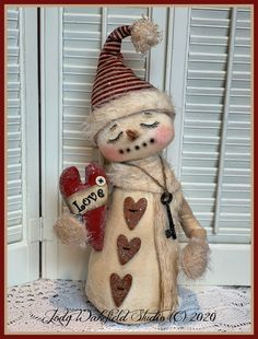 a stuffed snowman holding a red heart in his hand with the word love written on it