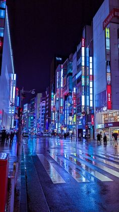 a city street at night with people walking on the sidewalk and buildings lit up in brightly colored lights