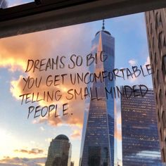 there is a message written on the window in front of skyscrapers that say, dreams so big you get uncomfortableable telling small minds people