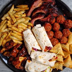 a black plate topped with lots of tacos and meats next to french fries