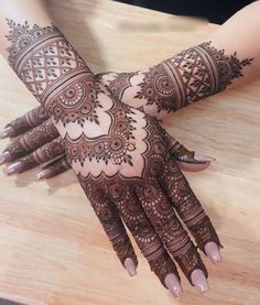 two hands with henna tattoos on them sitting on a wooden table next to a knife