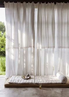 a bed sitting under a window next to a white curtain