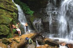 three people standing at the base of a waterfall with backpacks on their shoulders and one person taking a photo