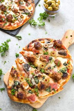 two pizzas sitting on top of wooden cutting boards next to olives and parsley