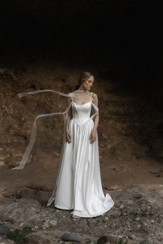 a woman in a white wedding dress standing on rocks with her veil blowing in the wind