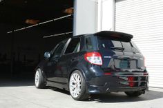 the back end of a small black car parked in front of a garage with its door open