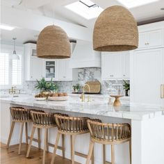 a kitchen with white cabinets and wooden stools in front of an island topped with marble counter tops