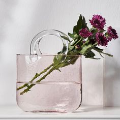 a pink bag with flowers in it sitting on a white shelf next to a vase