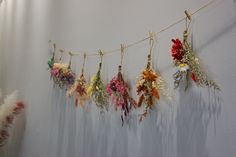 flowers are hanging on a string in front of a white wall and some feathers hang from it