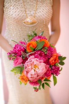 a bride holding a bouquet of pink and orange flowers on her wedding day in front of a wall