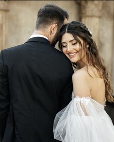 a man in a tuxedo and a woman in a wedding dress smile at each other