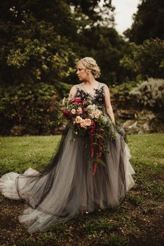 a woman standing in the grass wearing a gray and black dress with flowers on it