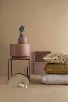 a stack of pillows and other decorative items on a pink surface with a cactus in the background