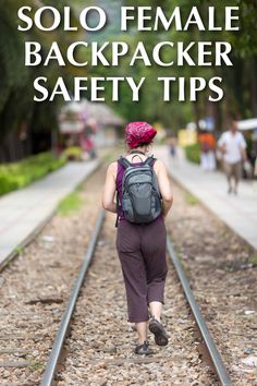 a woman with a backpack walking down train tracks in the middle of town on a sunny day