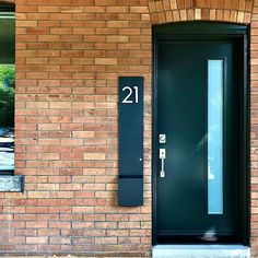 a black door is on the side of a red brick building and numbers are displayed