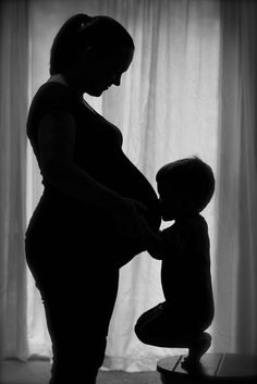 a pregnant woman holding her child's hand while standing in front of a window