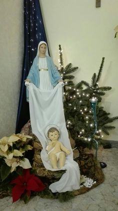 a statue of the virgin mary and baby jesus in front of a christmas tree with lights