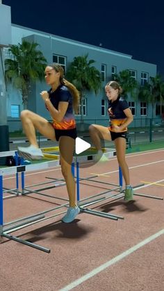 two women are sitting on hurdles in the middle of a race track, one has her leg up