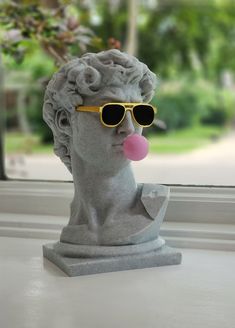 a statue with sunglasses blowing a bubble on it's nose while sitting in front of a window