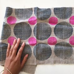 a person's hand on top of a piece of fabric with pink and grey circles