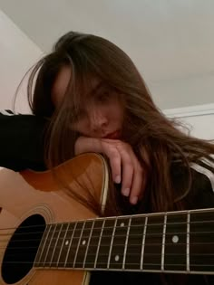 a woman with long hair holding a guitar in her hand and looking down at the camera