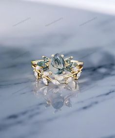 an engagement ring with green and white stones on the front, sitting on a marble surface