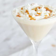 a drink in a martini glass topped with whipped cream, caramel and flakes