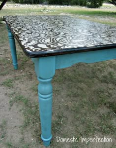 a blue table with black and white designs on it sitting in the middle of grass