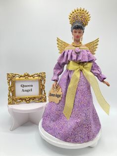 a purple and gold figurine next to a small white table with a sign that says queen angel on it