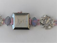 A new ladies wrist watch with the strap replaced by a silver coloured fashion jewellery bracelet, length approx. 200mm (8 ins). The watch was bought new and the bracelet was designed and assembled by hand. The watch is contained in a rectangular silver coloured metal case (approx. 22mm x 24mm).  The face is white with silver coloured pointers and quarter hour markers. The round links of the bracelet are of silver coloured metal scrollwork with a floral theme, inset with round pearlescent white b Adjustable Silver Jewelry And Watches With Round Dial, Silver Watch As A Gift, Silver Watches Suitable For Gifts, Adjustable Metal Bracelet Watch, Rectangular Silver Metal Watch, Adjustable Silver Bracelet Strap Jewelry And Watches, Silver Rectangular Metal Watch, Silver Metal Bracelet Strap Watch, Adjustable Silver Analog Jewelry And Watches