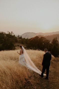 a bride and groom walking through tall grass