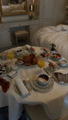 a table with breakfast food on it in front of a mirror and dresser next to a bed