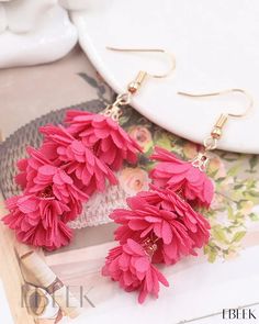 the pink flower earrings are on display next to a white plate with flowers in it