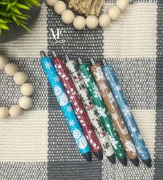 four different colored pens sitting on top of a checkered table cloth next to a potted plant