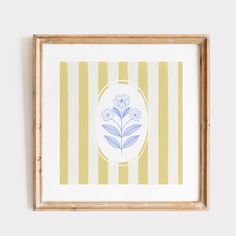 a blue and white flower is on a yellow striped background in a wooden frame hanging on the wall