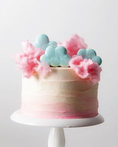 a white cake with pink and blue frosting on top is sitting on a pedestal